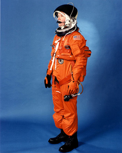 Vemos una persona con traje espacial color naranja  y con un casco diferente guantes y botas negras